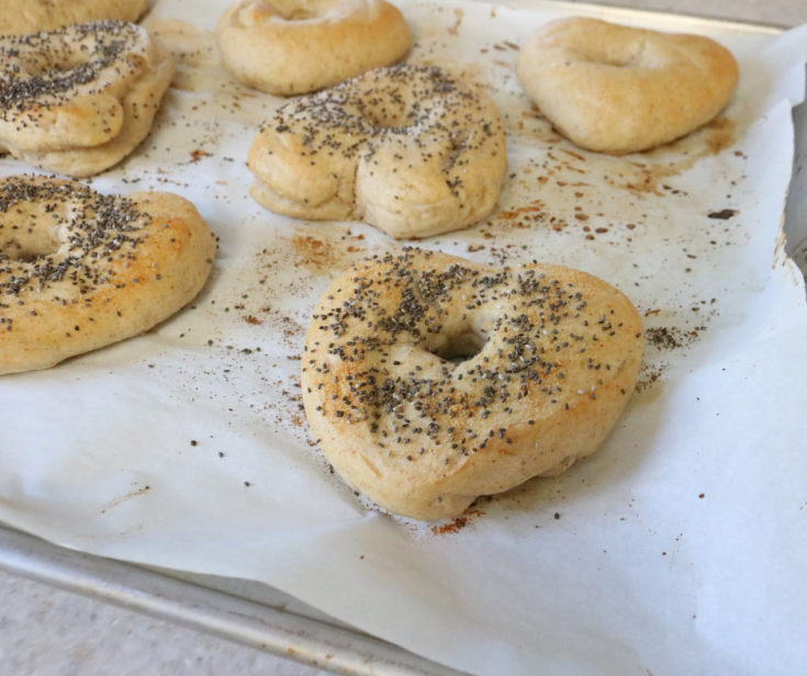 7 heart shaped baked bagels with a slightly golden crust sitting on top of a cookie tray lined with parchment paper