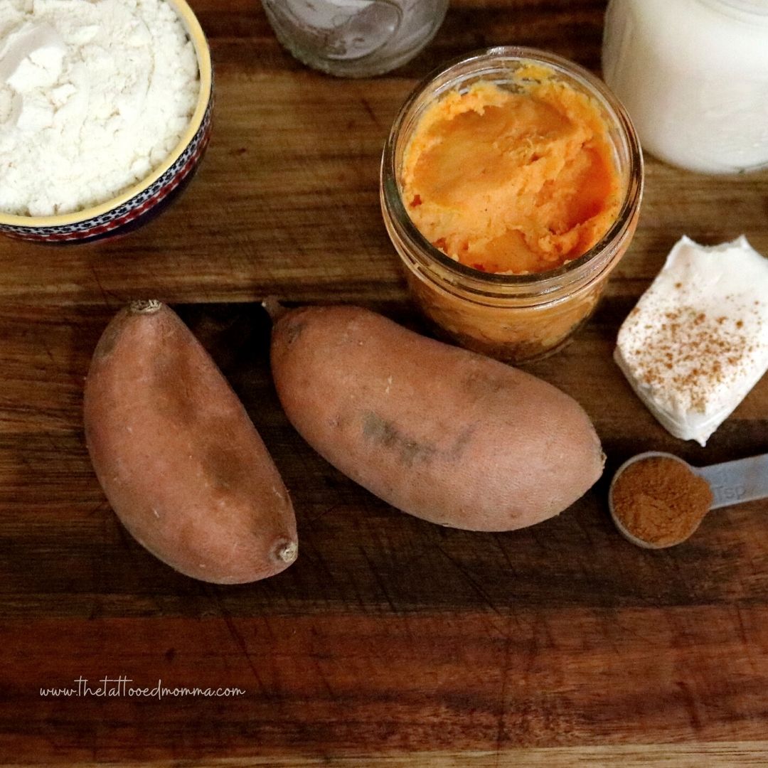 cooked sweet potatoes in mason jar with 2 raw ones next to it sitting on a wooden cutting board